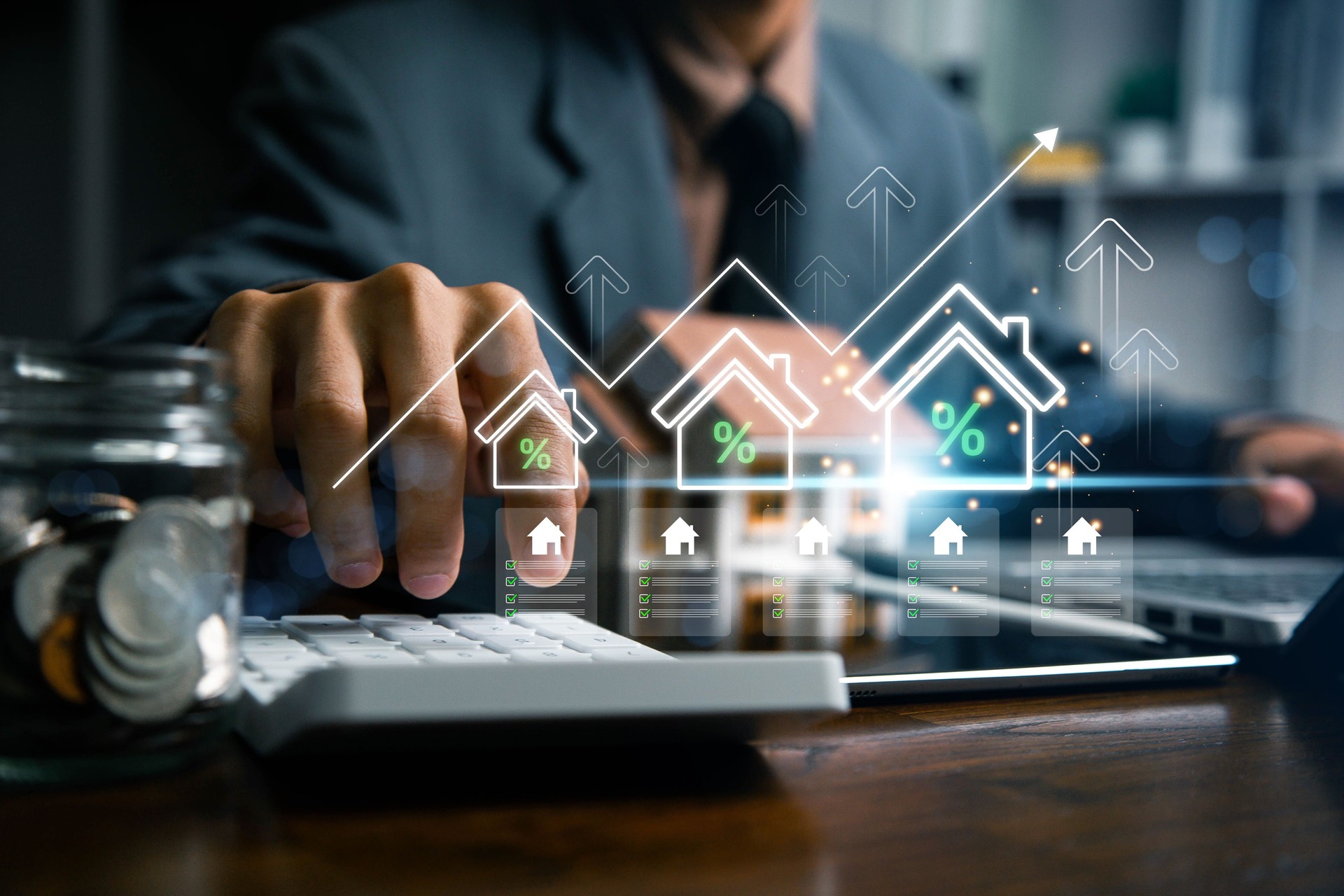 Real estate investment and mortgage calculation concept with businessman using calculator, coins stacked on desk, laptop, and small house model, representing property finance, budget planning, and home loan.